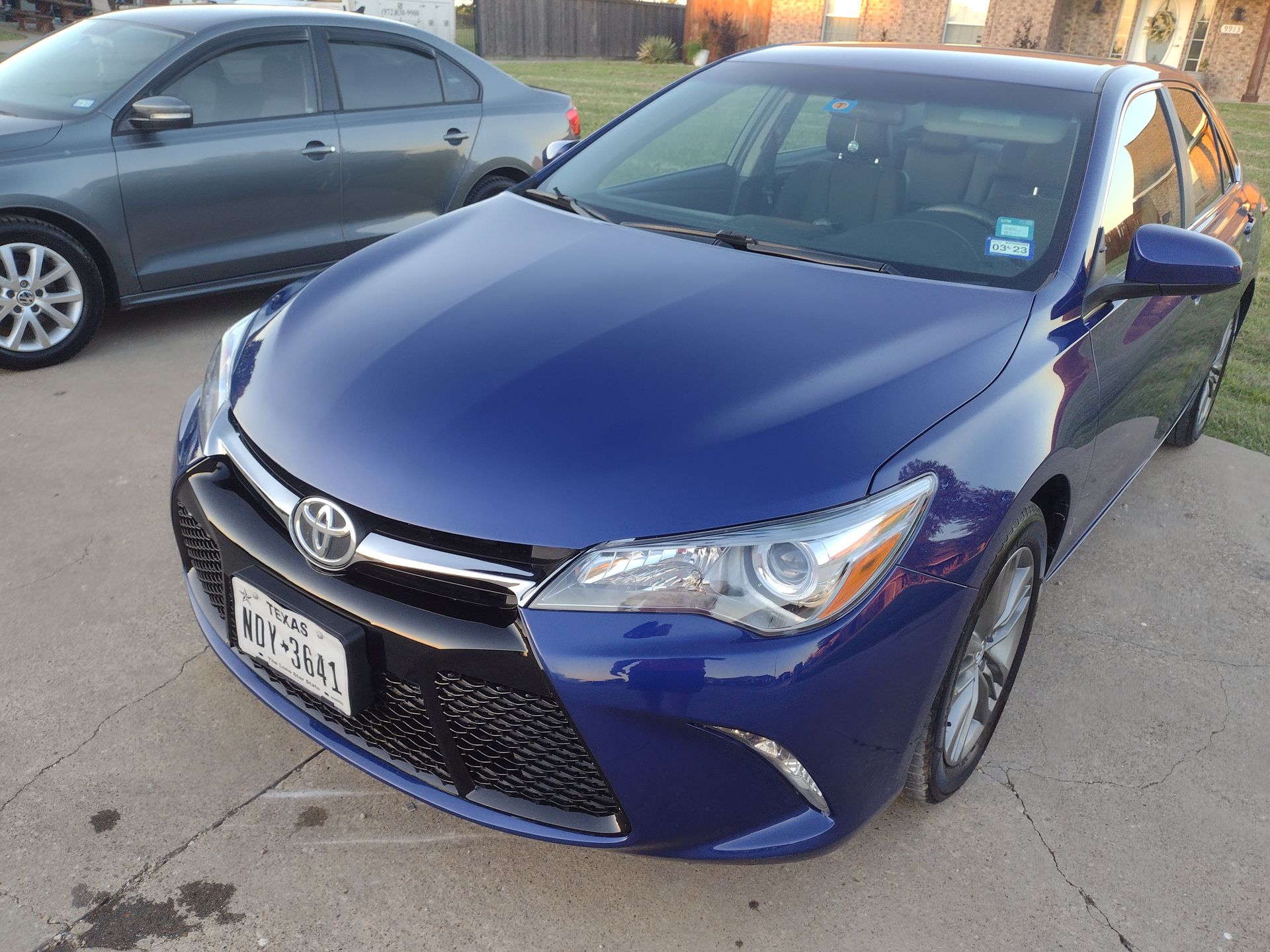 Blue Toyota Camry parked on a concrete driveway, a gray car in the background.
