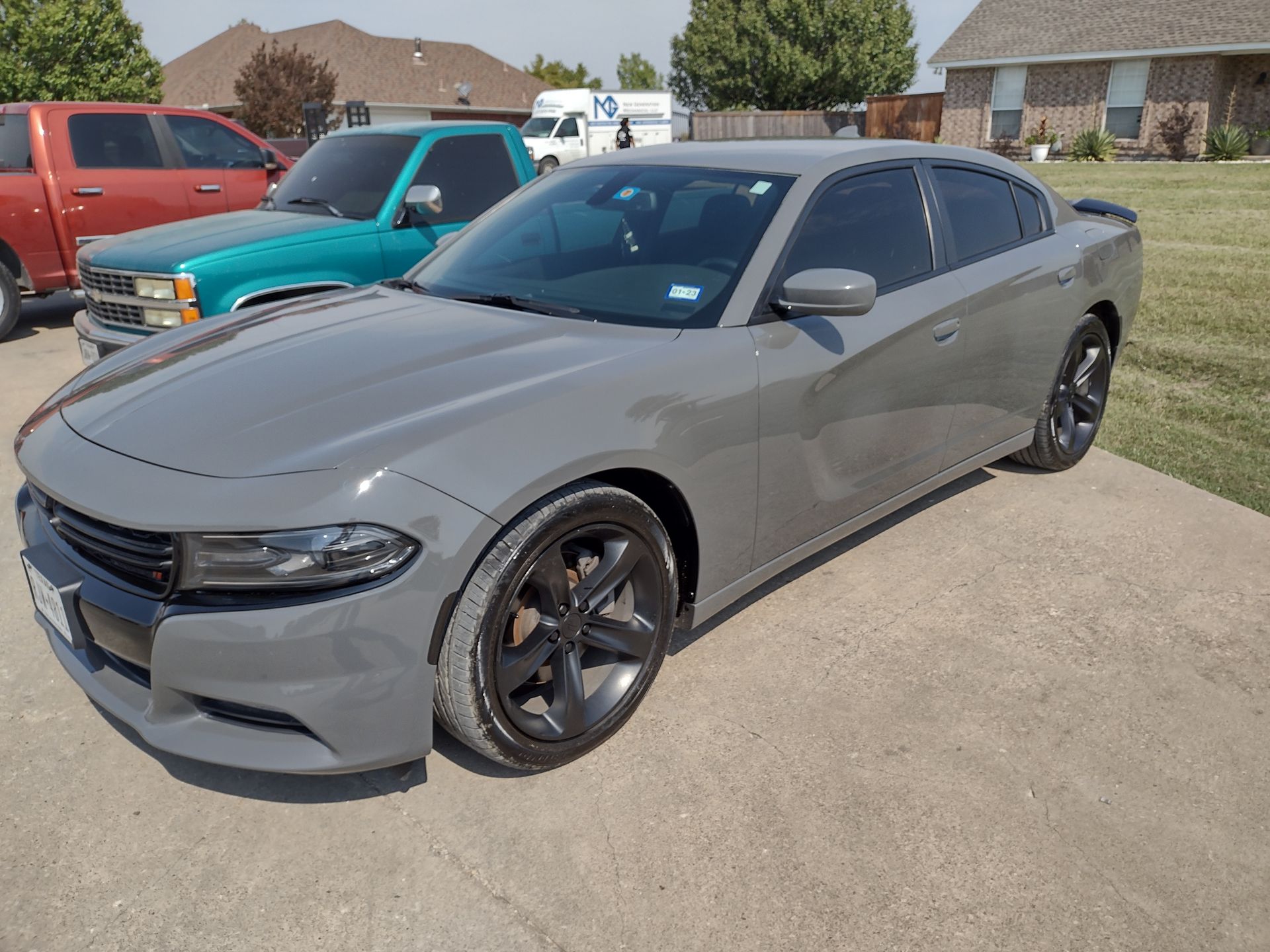 Gray Dodge Charger parked on a driveway with other vehicles and a house in the background.