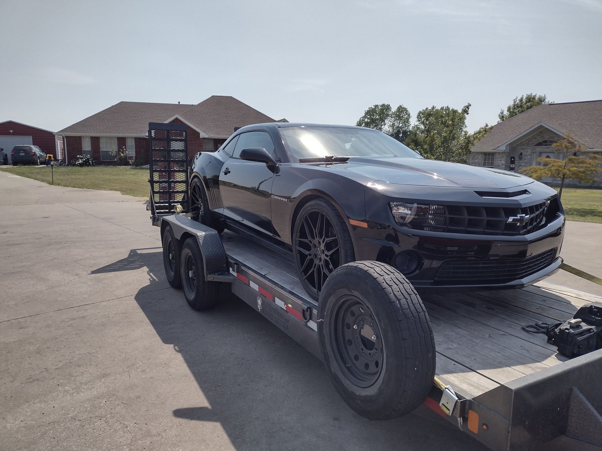 Black Camaro sports car on a flatbed trailer on a sunny day.