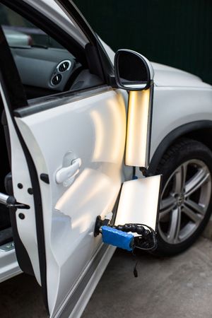 White car door with dent being repaired using lights and tools.
