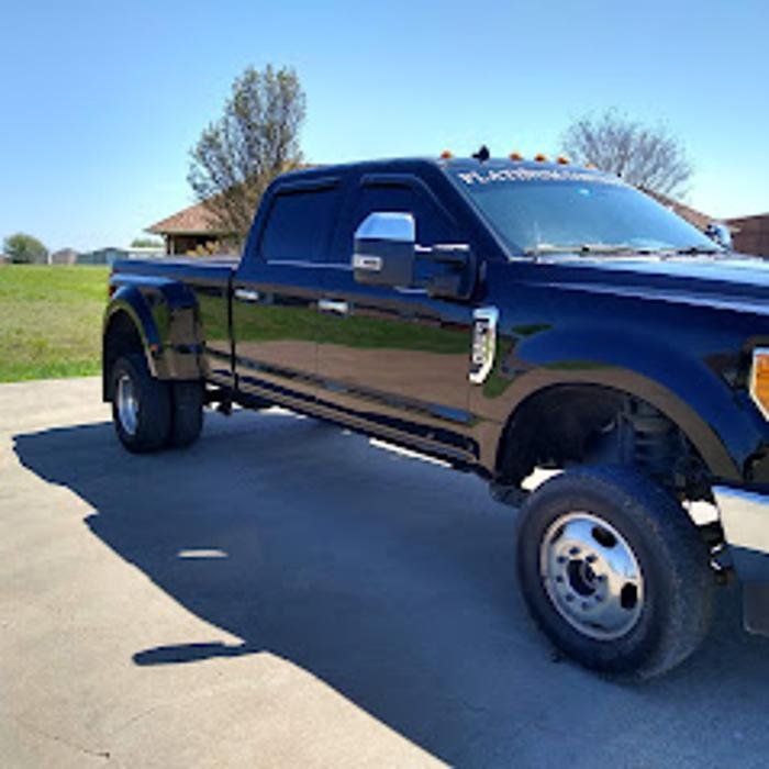 Black Ford F-350 dually pickup truck parked on a paved surface on a sunny day.