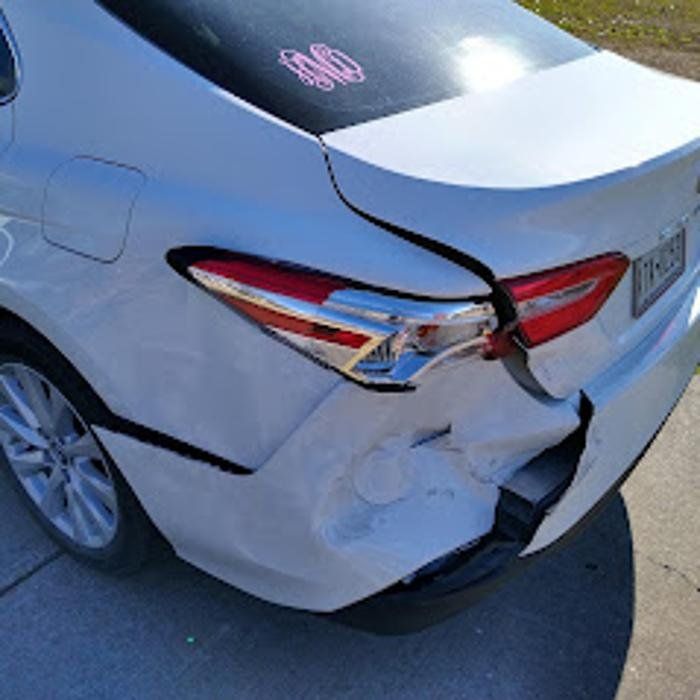 White car with significant rear-end damage, including dented bumper and broken taillight.