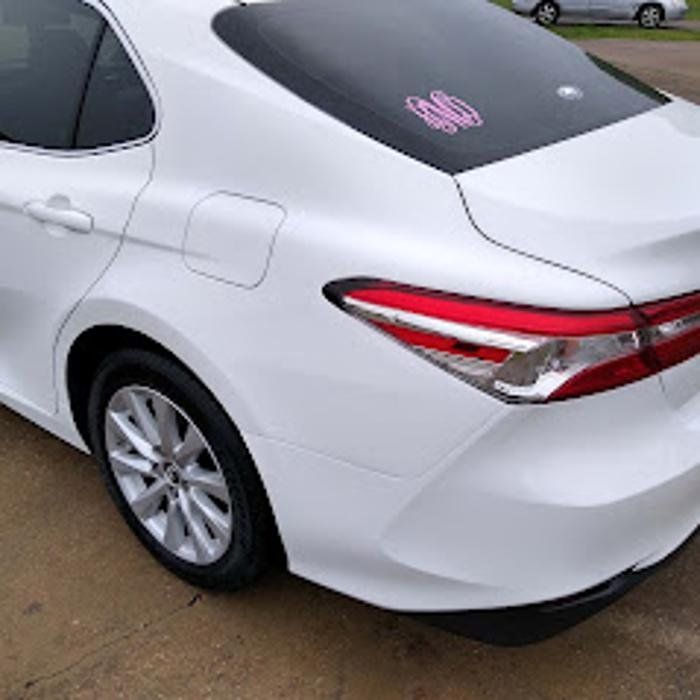 White car's rear quarter panel and tail light. Includes a sticker on the back window and a wheel.