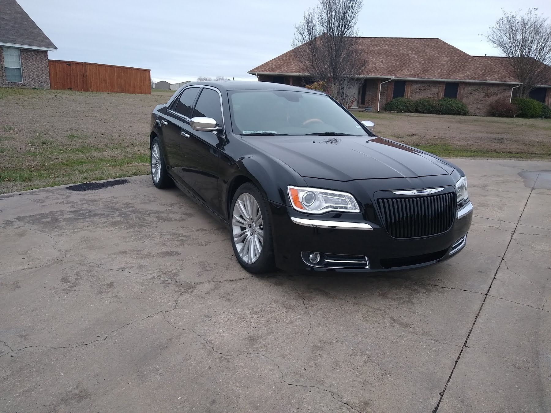 Black Chrysler 300 sedan parked on a concrete driveway in front of a house.