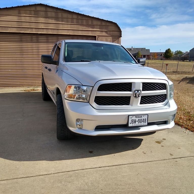 Silver Dodge Ram pickup truck parked in front of a tan garage on a sunny day.