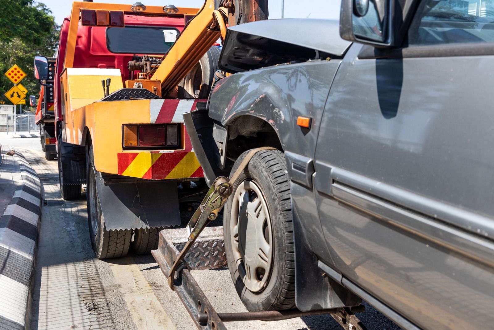Tow truck loading a damaged gray car onto its flatbed on a street.