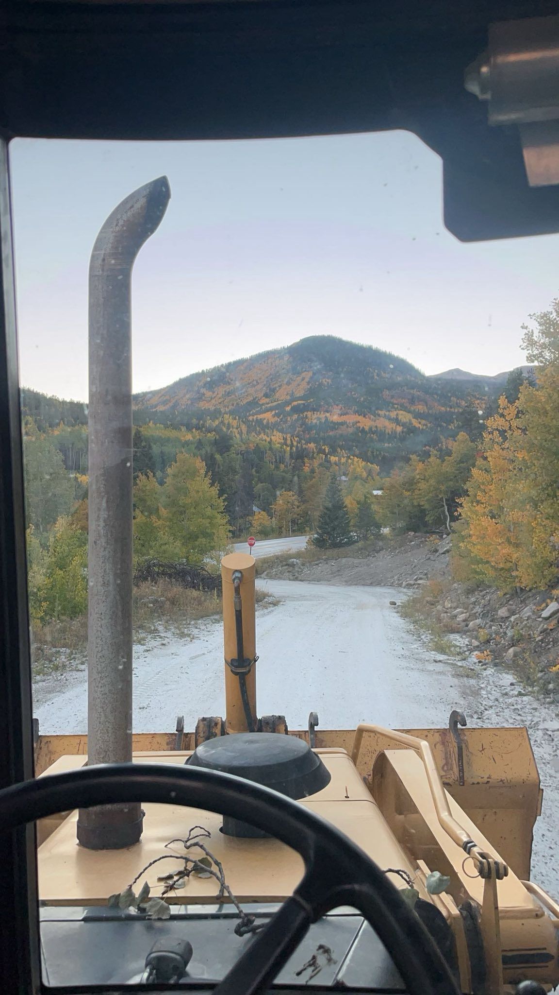 View from a vehicle cab overlooking a river, autumn hills, and a distant mountain.