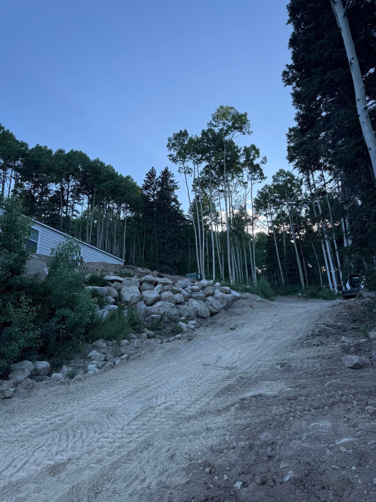 Gravel road winding uphill beside stone wall and tall trees under a blue evening sky