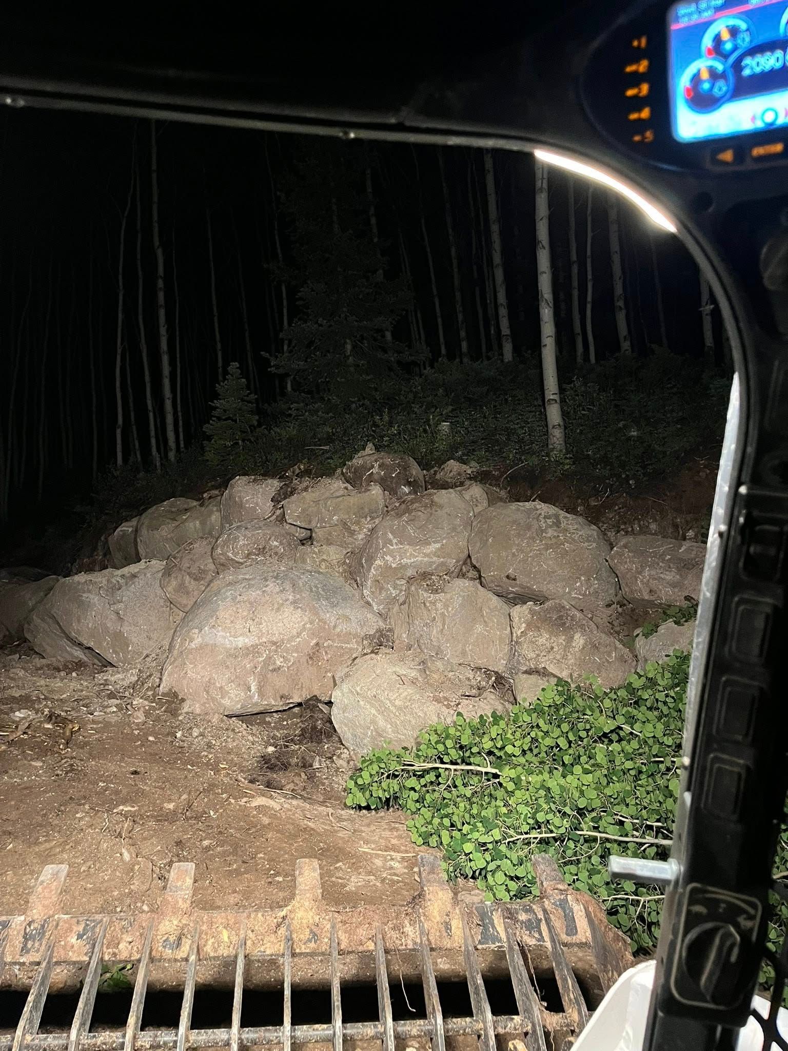 Large dirt and rocks piled on a roadside at night, viewed from inside a vehicle.