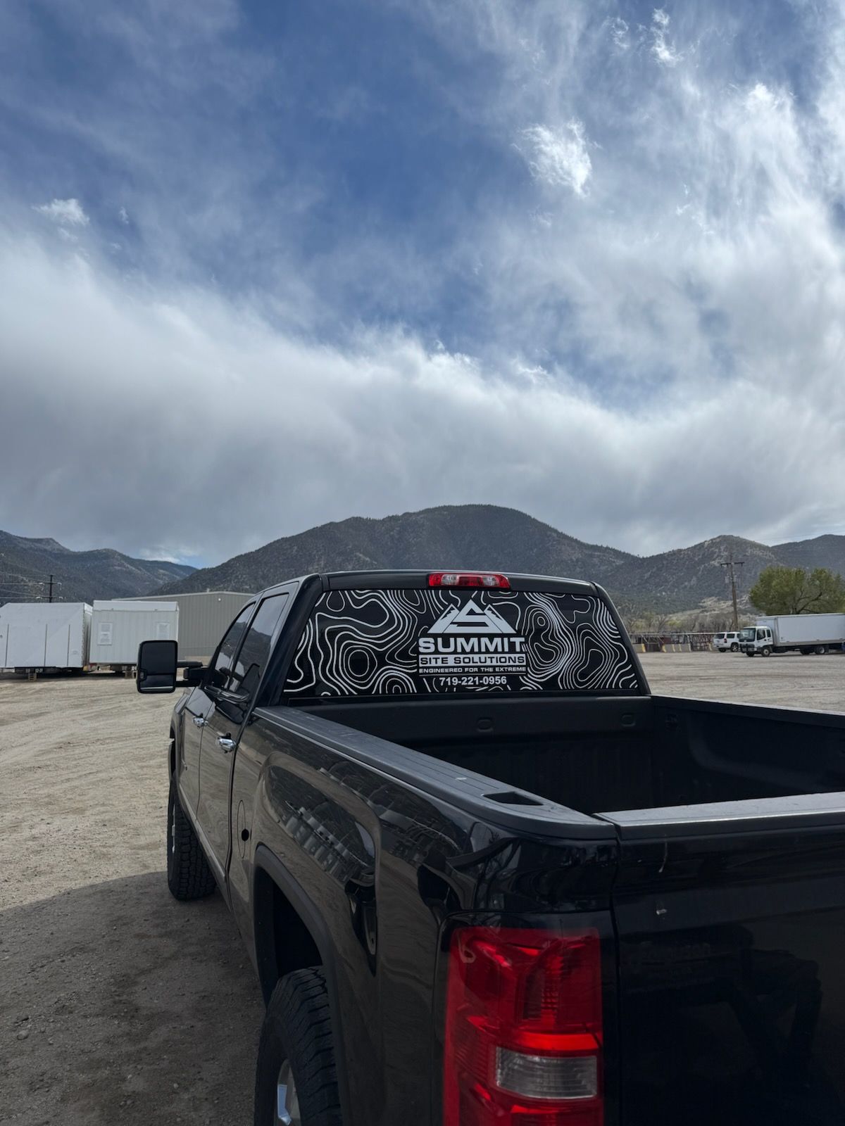 Black pickup truck parked on a sandy lot with mountains and cloudy sky in the background