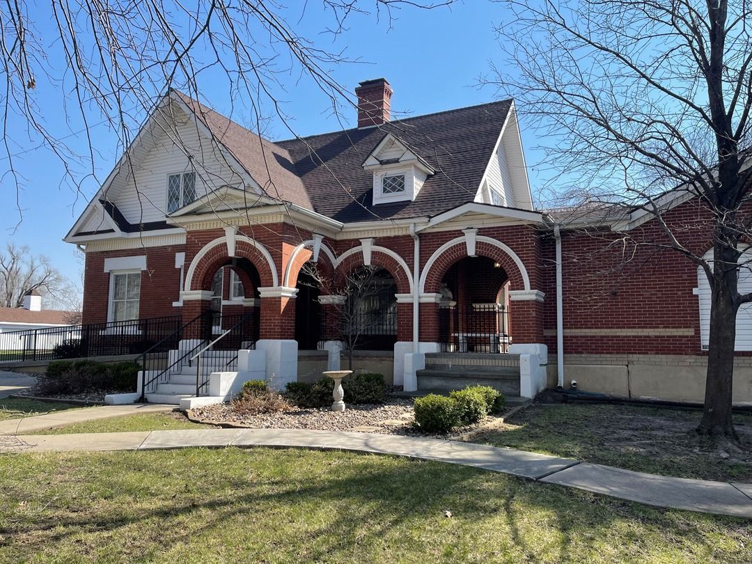 Brick house with arched porch, white columns, and a gabled roof on a sunny day