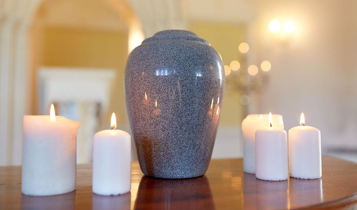 White candles surround a blue ceramic urn on a wooden table in a softly lit room