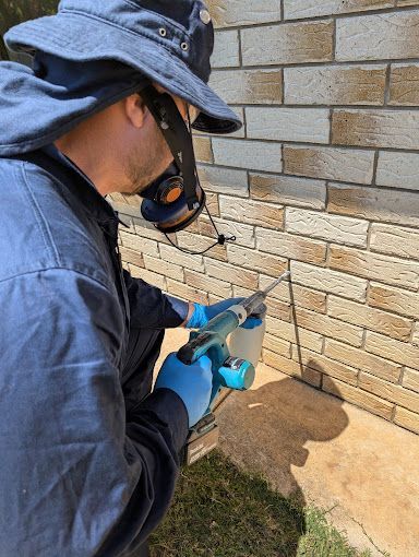 A Man is Spraying a Brick Wall With a Sprayer — Total Pest and Carpet Cleaning in Yeppoon, QLD