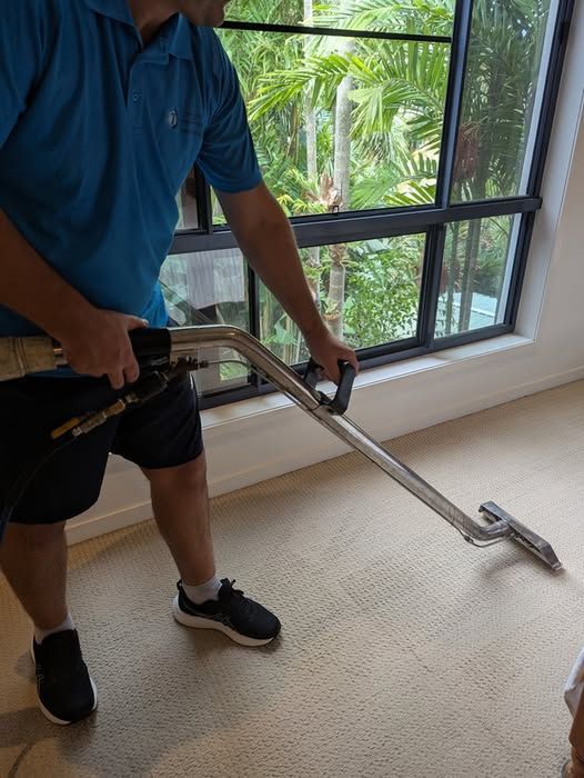 A Man is Cleaning a Carpet With a Vacuum Cleaner — Total Pest and Carpet Cleaning in Yeppoon, QLD