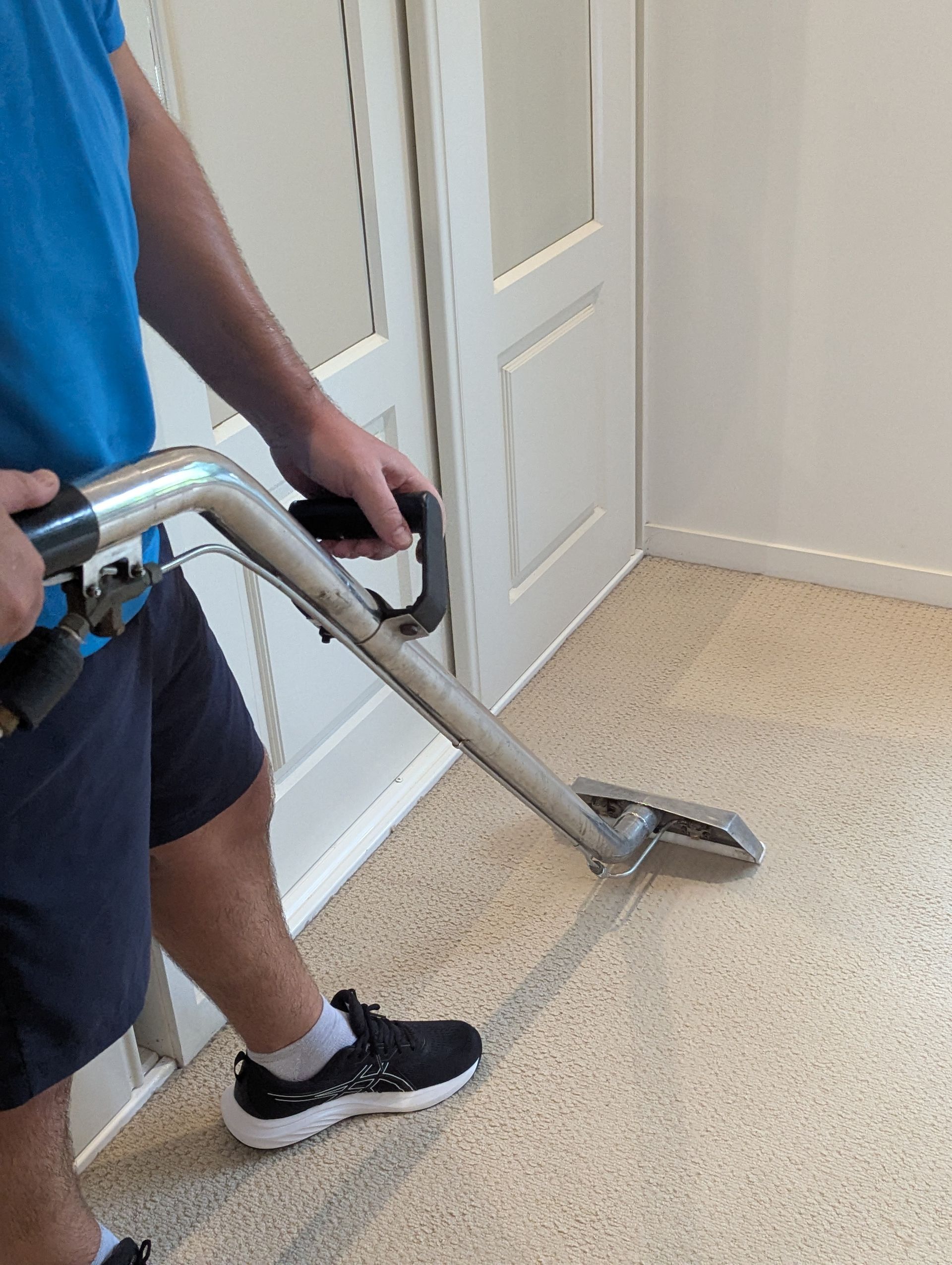 A Man Is Cleaning A Carpet With A Vacuum Cleaner— Total Pest and Carpet Cleaning in Yeppoon, QLD