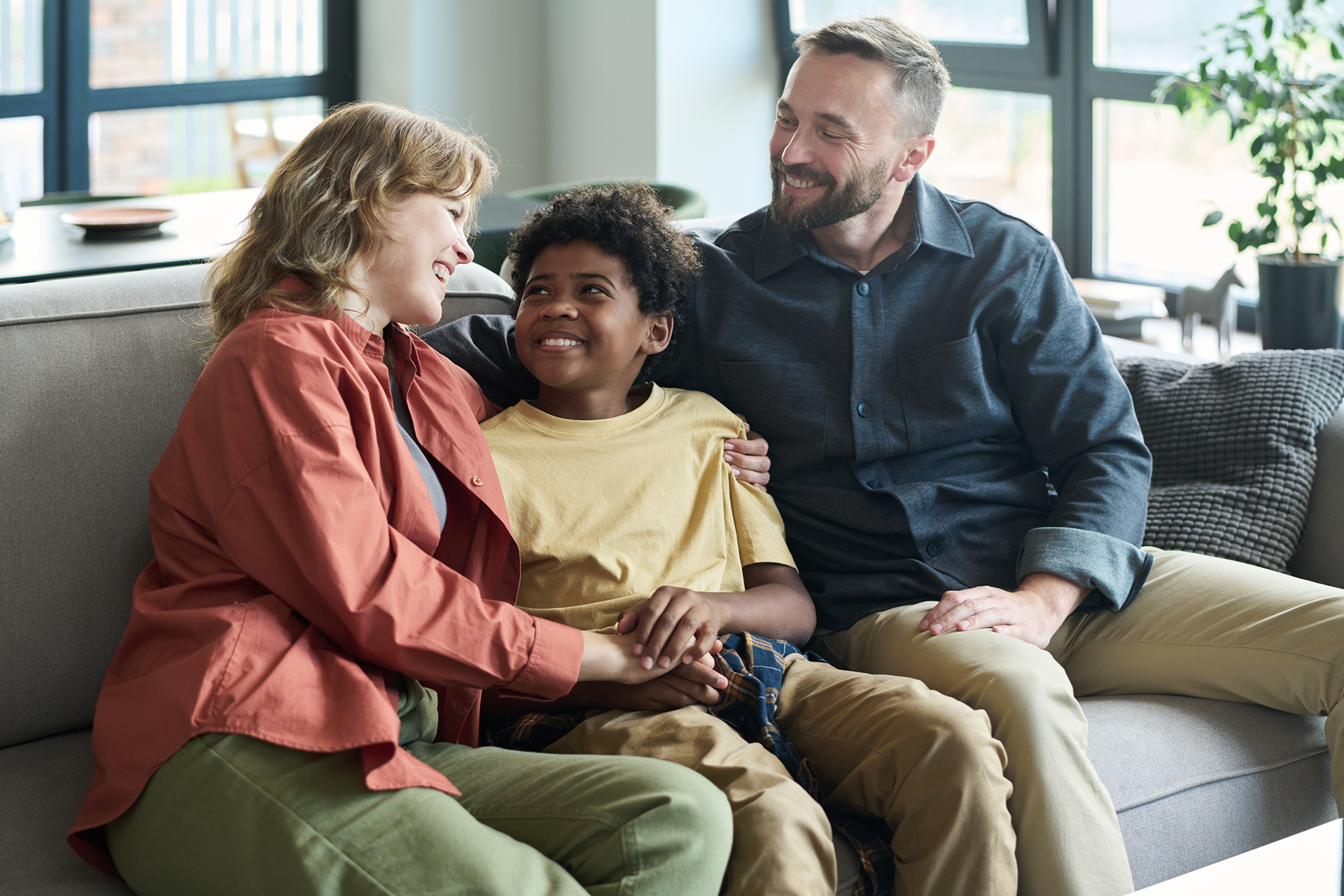 Family of four sitting on a blanket in front of a white RV on a sunny day.