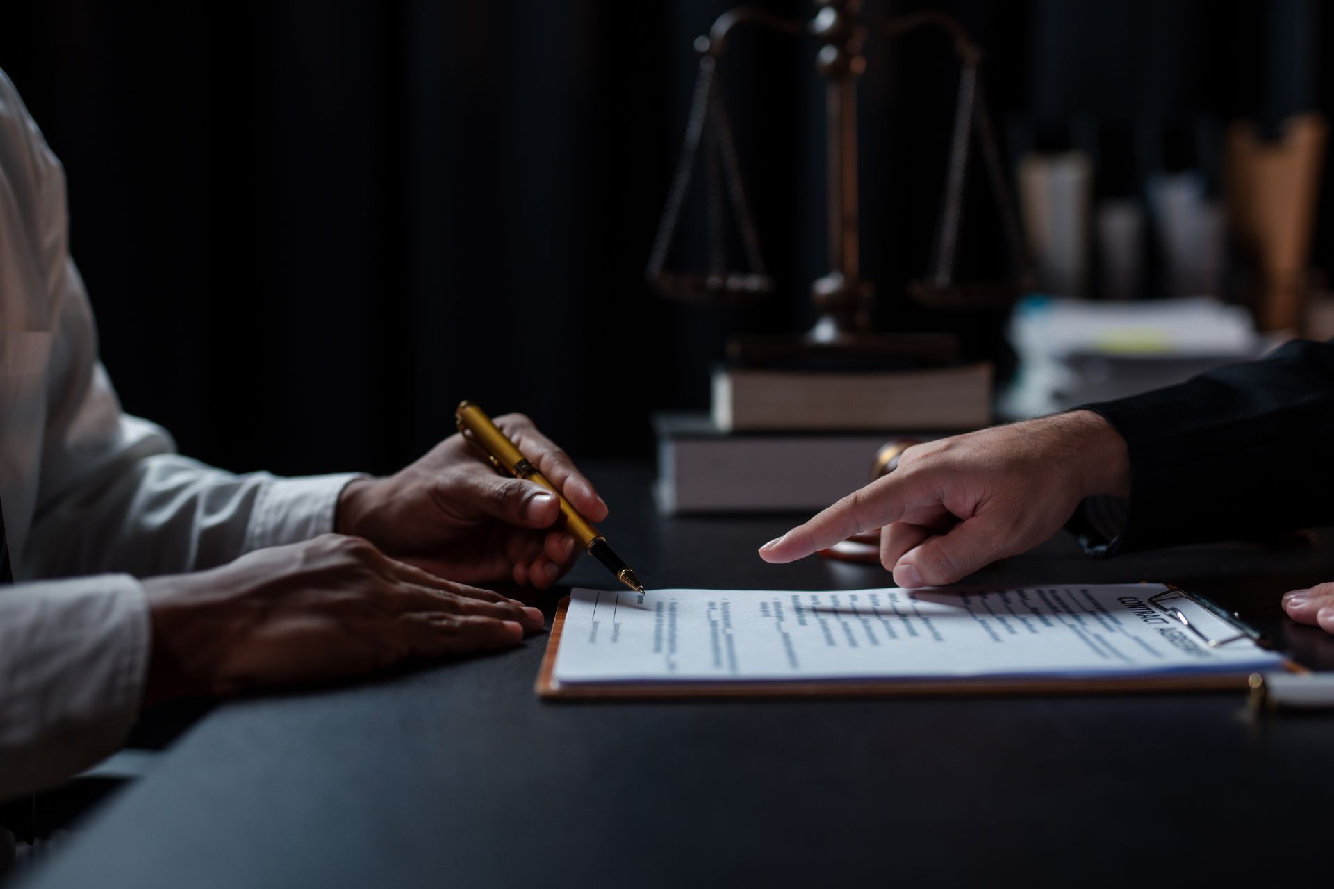 Lawyer pointing to a document on a clipboard during a consultation. Gavel, scales of justice, and books are on the table.