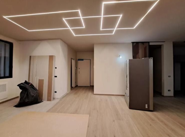 Camera moderna non arredata con pavimento in legno chiaro e lampade a soffitto geometriche.