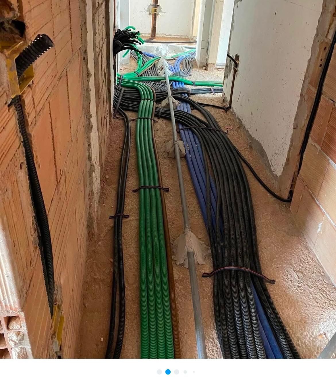Corridoio di cantiere con fasci di cavi verdi, blu e neri che corrono lungo il pavimento verso una porta.