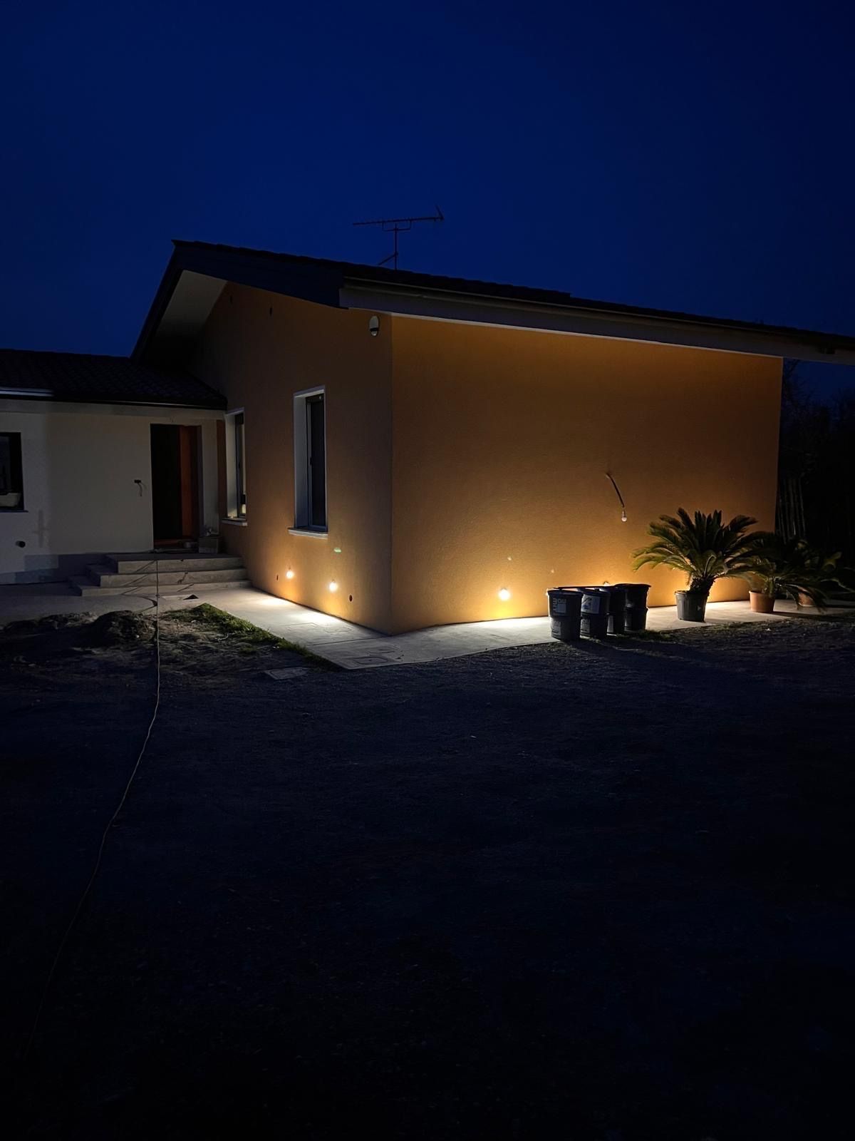 Esterno della casa di notte con luci calde del portico e vialetto d'accesso buio