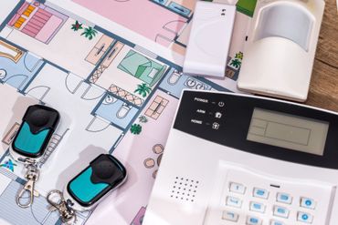 Configurazione del sistema di sicurezza domestica con planimetria, pannello di controllo dell'allarme, sensori e telecomando su una scrivania.