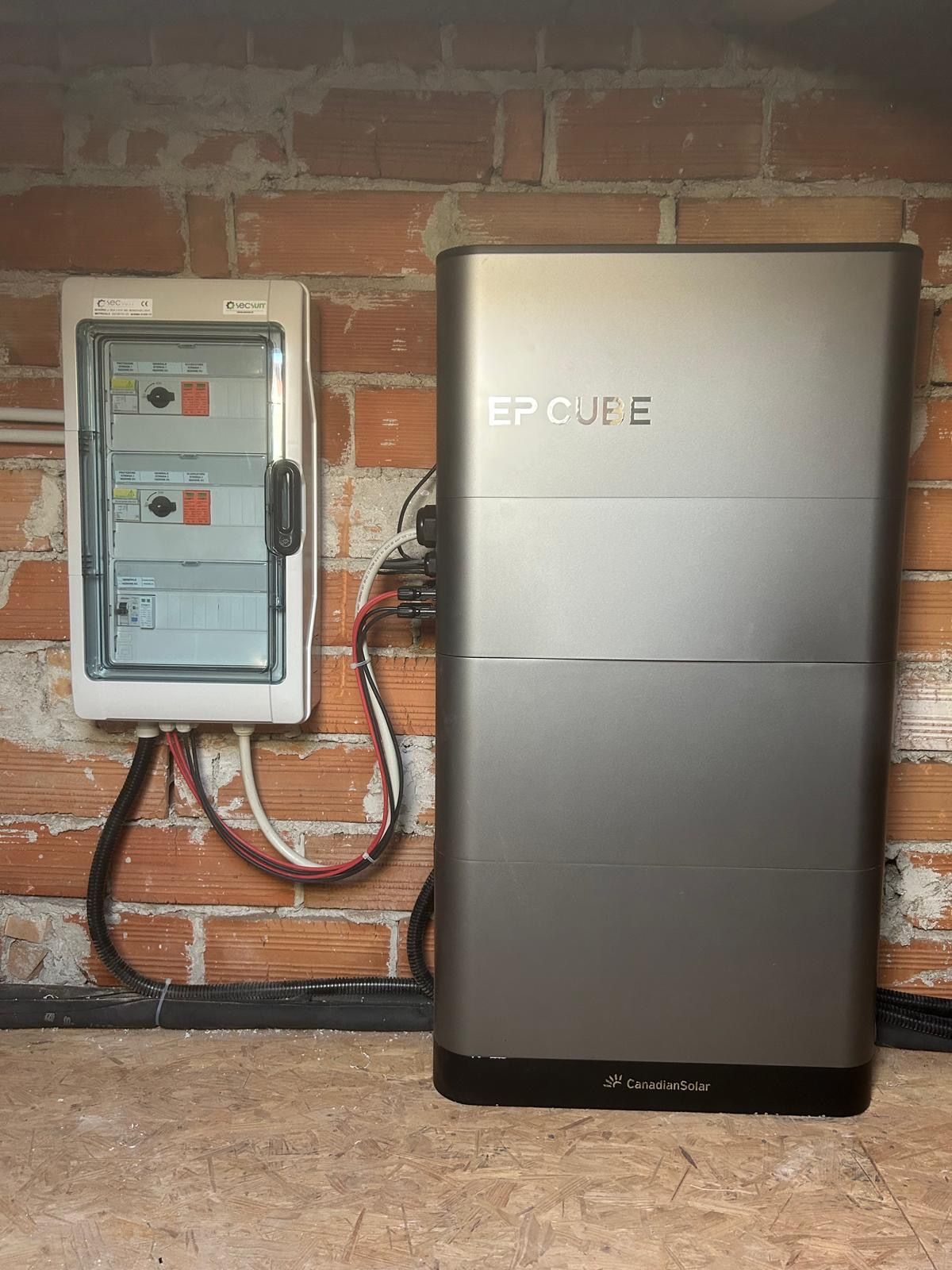 Pannello elettrico a parete accanto a un'unità di backup a batteria di colore argento, addossata a un muro di mattoni.