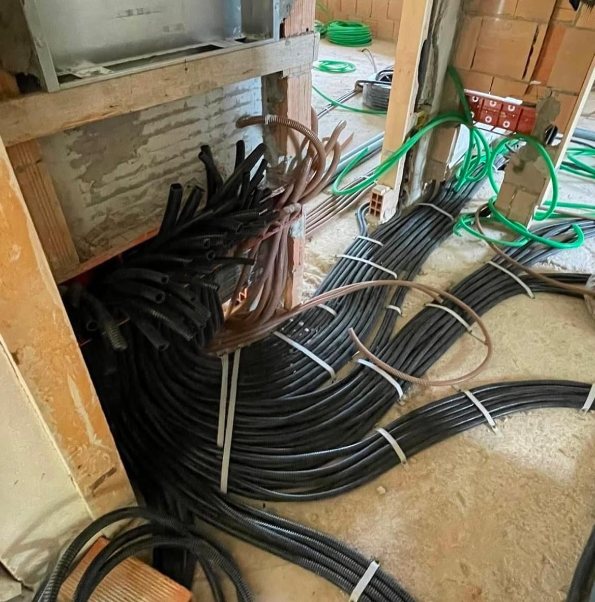 Cavi neri e marroni arrotolati e raggruppati sul pavimento di un locale tecnico o di un'area di cablaggio non rifinita.