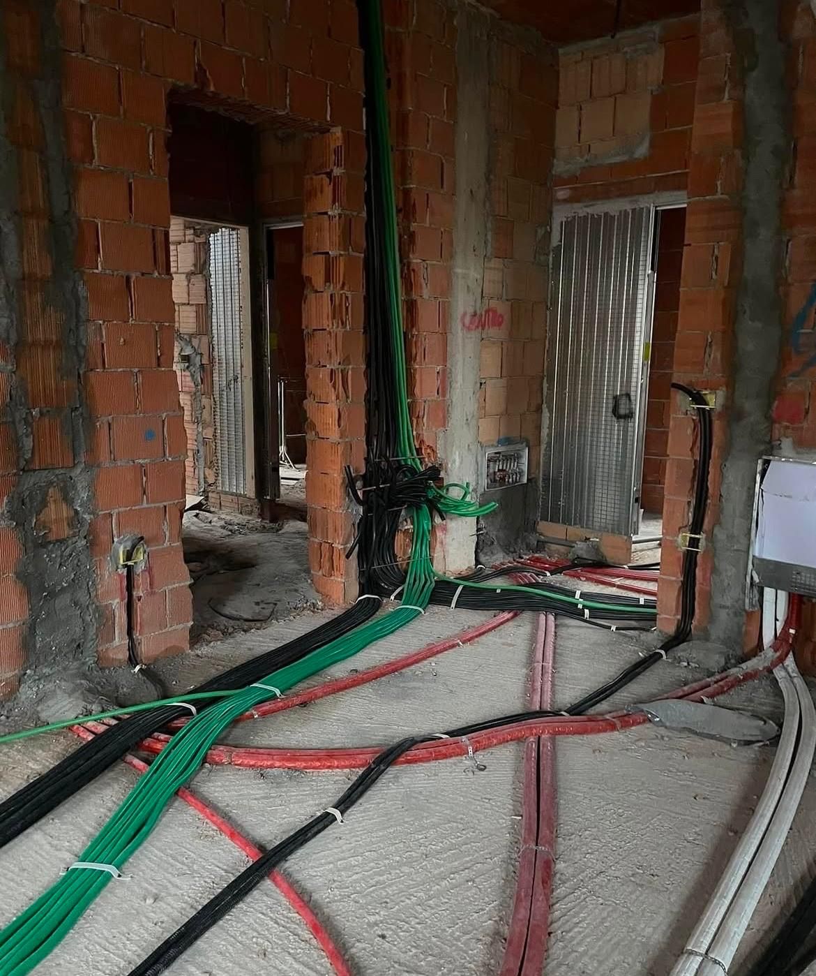 Interno in mattoni non rifiniti con cavi e tubature a vista su pavimento in cemento.