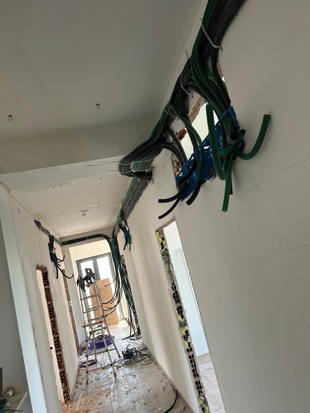 Soffitto del corridoio danneggiato con cavi scoperti e detriti, vista verso una stanza danneggiata in lontananza.