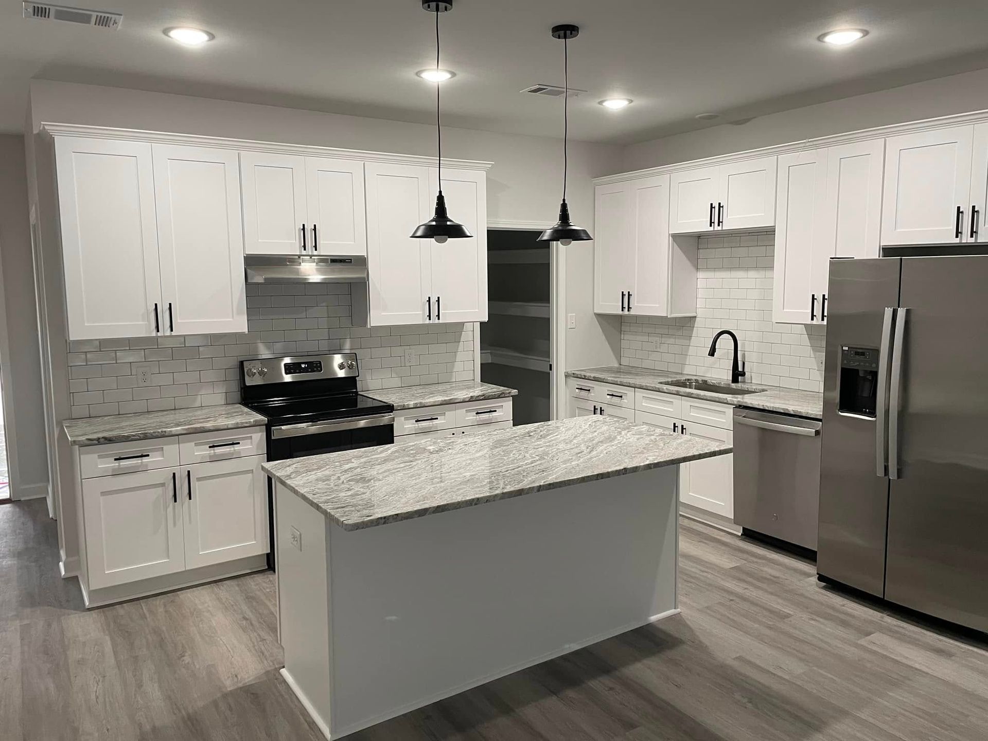 A kitchen with white cabinets , granite counter tops , stainless steel appliances and a large island.