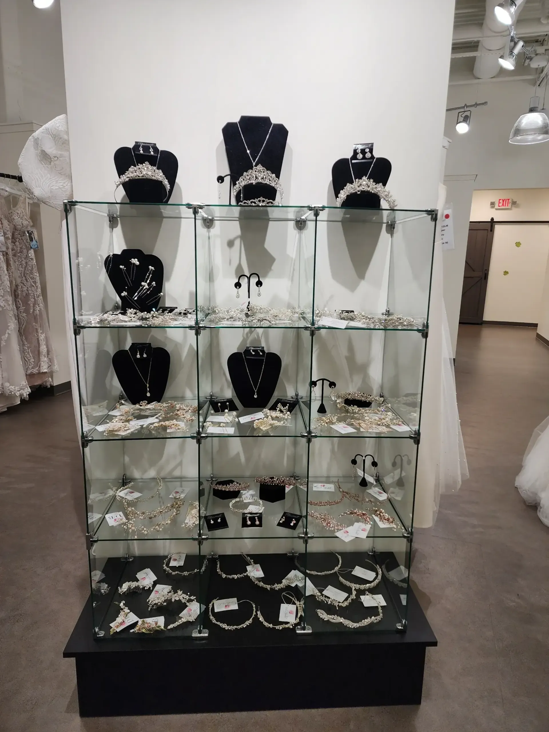 Jewelry display case in a bridal shop. Necklaces, earrings, and headpieces on black mannequins and glass shelves.