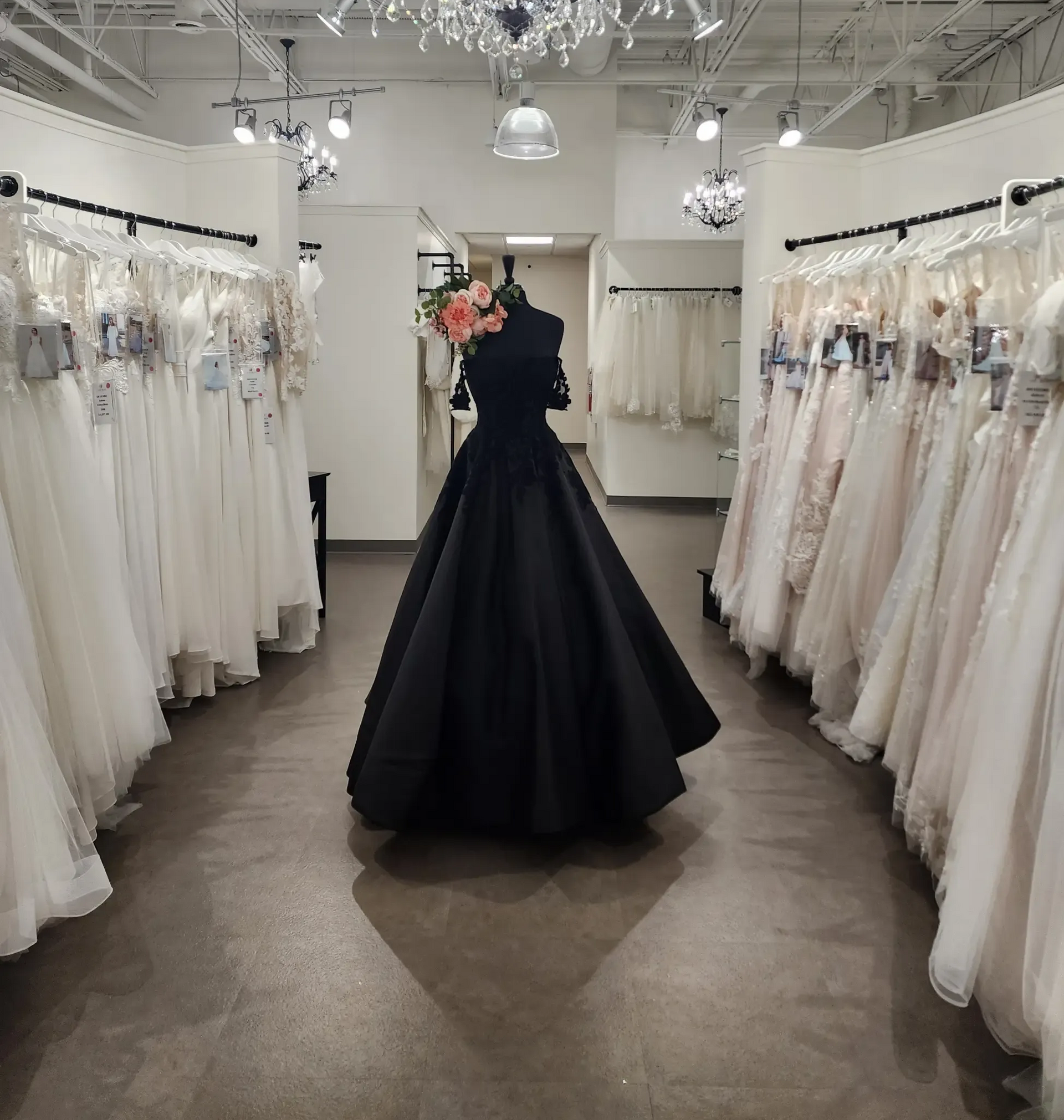 A black ball gown on a mannequin, surrounded by wedding dresses in a bridal shop.