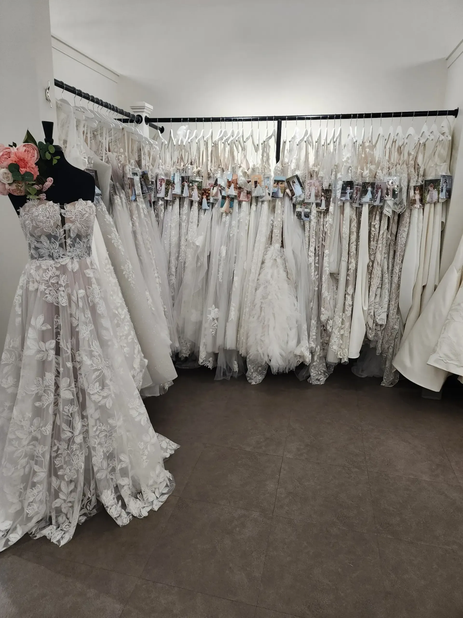Wedding dresses hanging on racks in a bridal shop, one displayed on a mannequin.