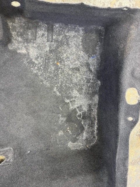 Gray car carpet with white mold patches in a rectangular area, possibly from water damage.