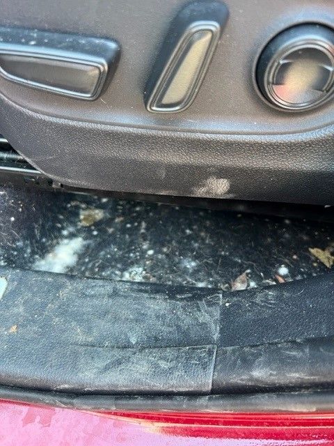 Close-up of a car seat with power adjustment controls, revealing a dirty interior with white specks on the floor.