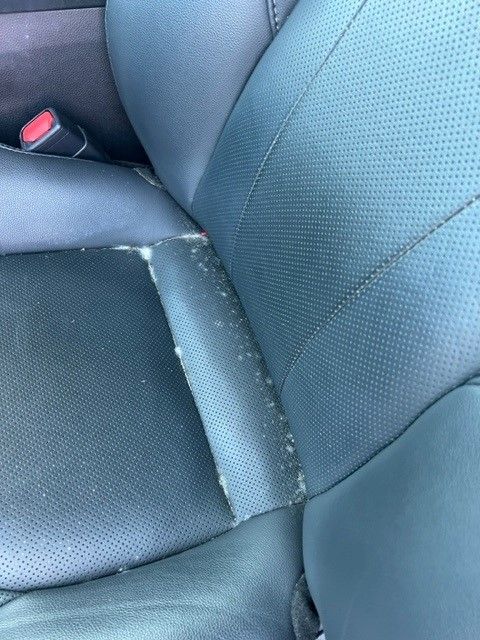 Close-up of a car seat with cracked, worn black leather. The damage is focused on a seam.