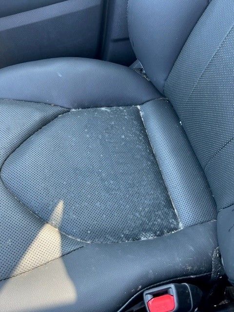 Black car seat with significant wear and flaking on the center cushion.