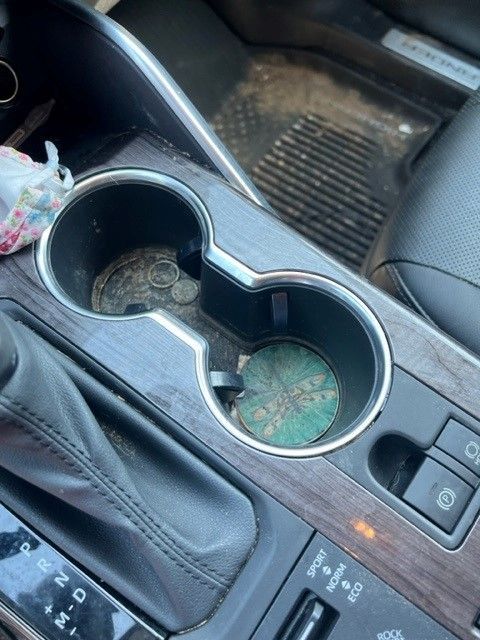 Close-up of a car's center console with dirty cup holders. One has coins, the other a green coaster.