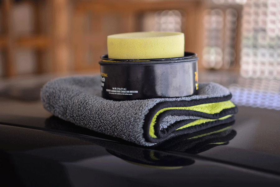Black car wax, applicator sponge, and microfiber towel on a car surface.