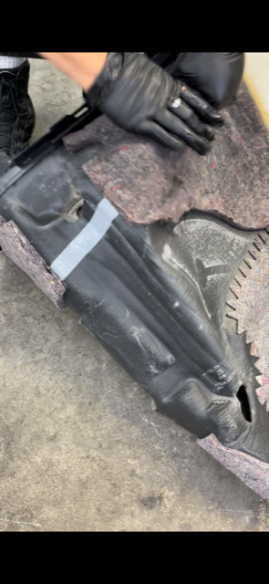 Person wearing black gloves working with a black plastic part, possibly a car component. Gray carpet.