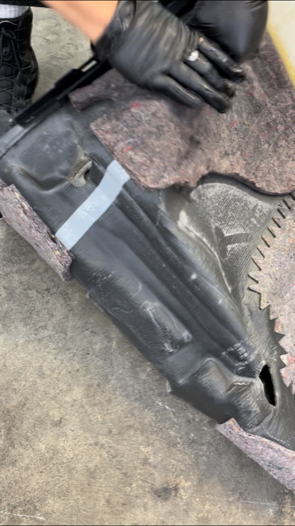 Person in black gloves works on a black plastic car part; gray tape applied.