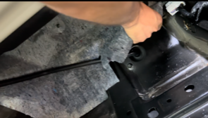 Person's hand reaching into a car's interior, near a black metal component and grey fabric.