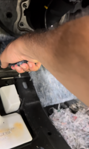 Person's hand grasping a dark object inside a vehicle's dashboard compartment, with foam padding visible.
