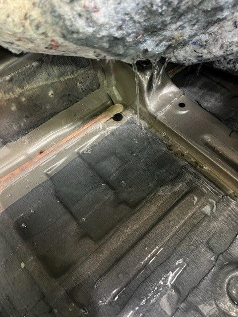 Bare car floor showing metal frame, water droplets, and car carpet remnants.