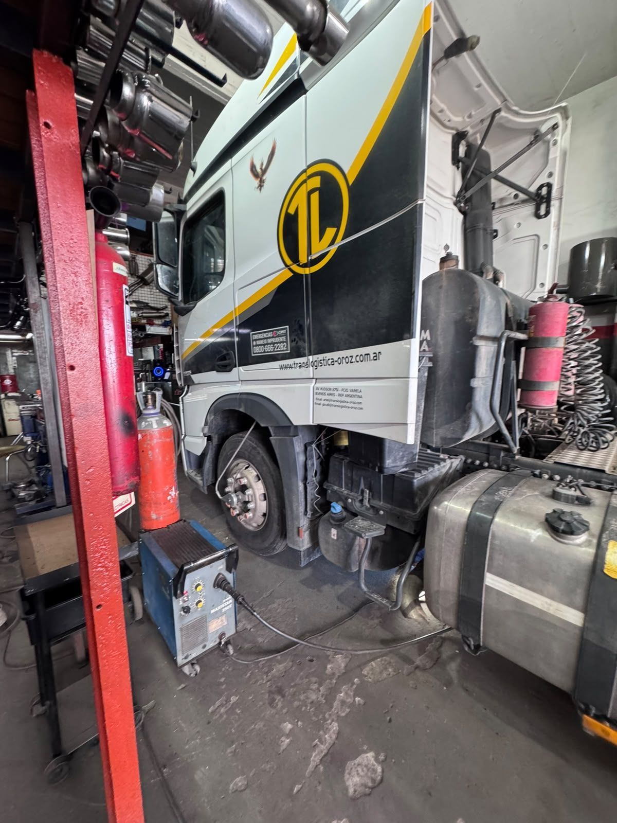 Truck parked inside a maintenance garage, with tool equipment and a red lift beside it.