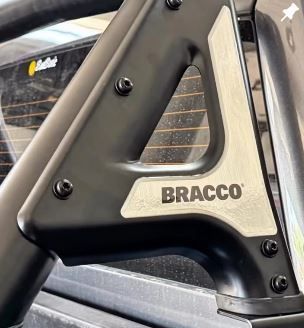 Primer plano de una pieza triangular negra para vehículos BRACCO con detalles y tornillos plateados.