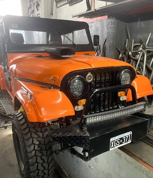 Jeep clásico de color naranja brillante con techo negro y neumáticos robustos estacionado en el interior de un garaje.
