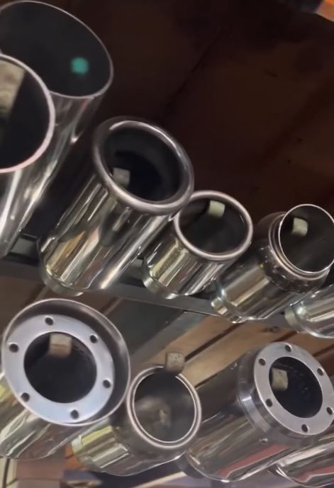 Tubos de escape cromados apilados en una vitrina, con bridas circulares visibles en un taller o tienda.