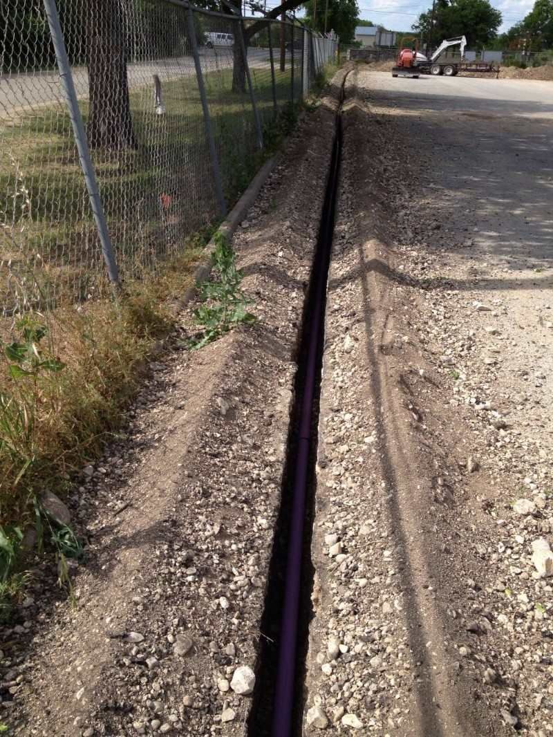 A purple pipe is laying in the dirt next to a fence.