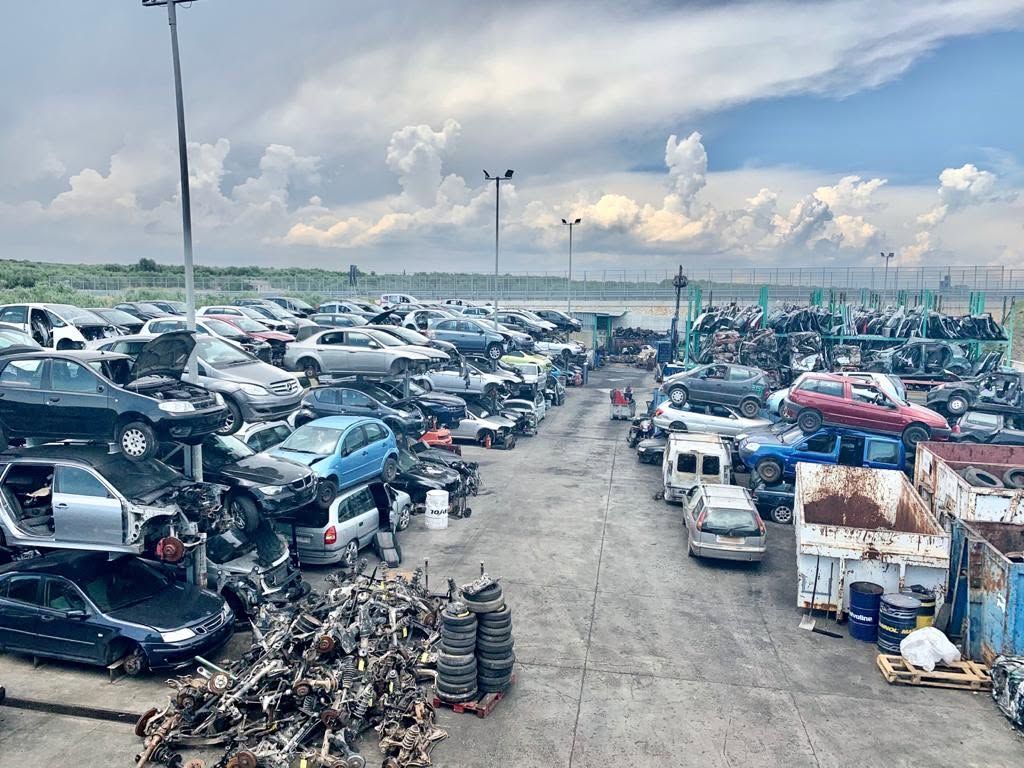 In un deposito di rottami, sotto un cielo nuvoloso, una fila di auto accartocciate si estende un paesaggio suggestivo